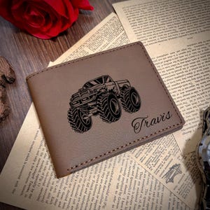 May include: A brown leather wallet with a black and white illustration of a monster truck and the name "Travis" engraved on the front.