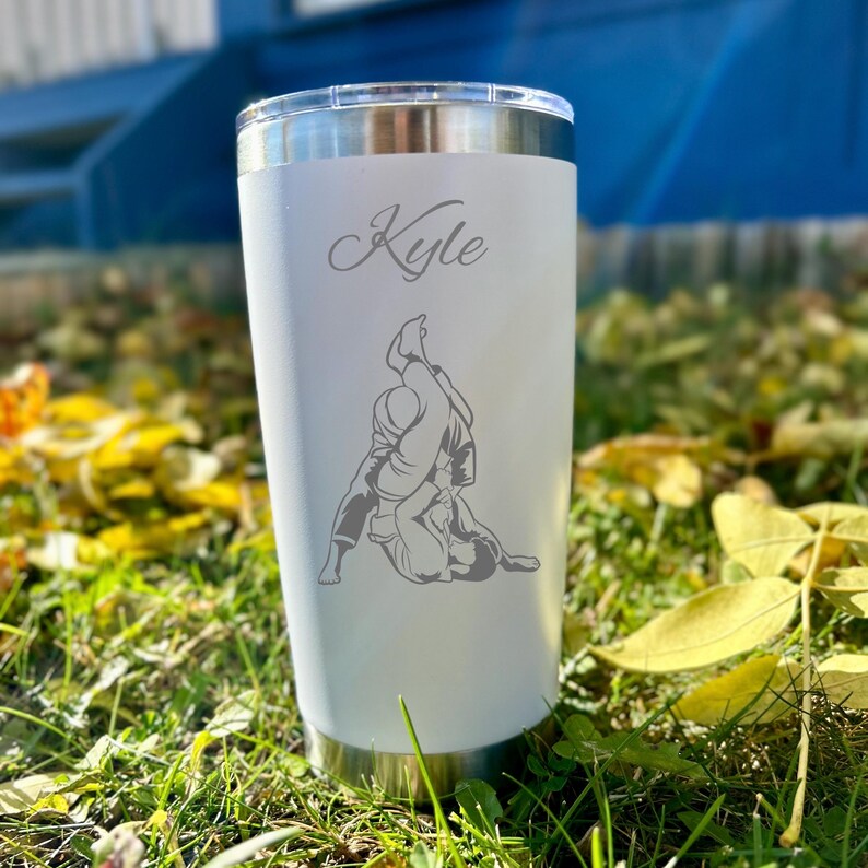 May include: White stainless steel tumbler with a gray engraved design of two people in a grappling position. The tumbler has the name "Kyle" engraved on the front.