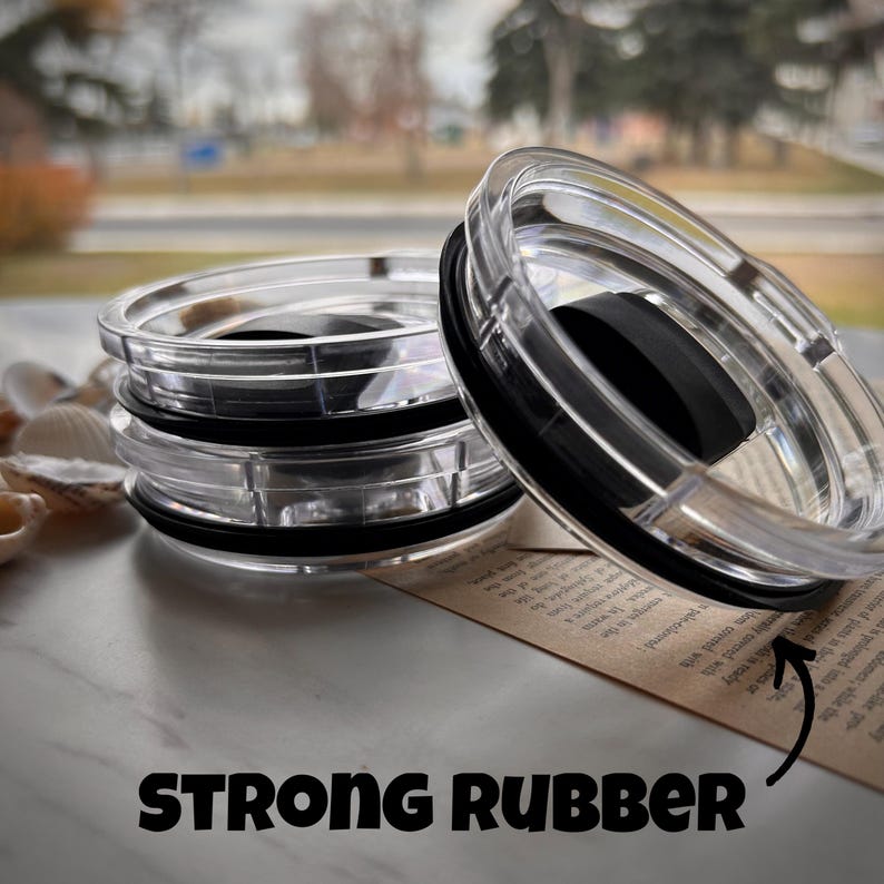 May include: Close-up of three clear plastic lids with a black rubber ring around the edge. The lids are stacked on top of each other. The text "STRONG RUBBER" is visible at the bottom of the image.