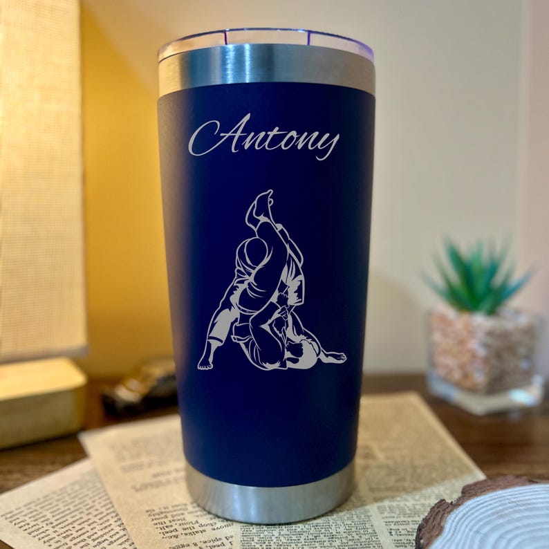 May include: A blue stainless steel tumbler with a white engraved design of two people in a grappling position. The name "Antony" is engraved above the design.