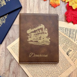 May include: A brown leather passport holder with a gold embossed image of a steam train and the name "Donovan" on the front.