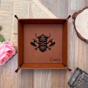May include: A brown leather valet tray featuring a Viking skull and crossed axes design. The tray is personalised with the name "Corey". Ideal for storing small items like keys and wallets.