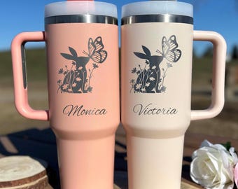May include: Two insulated travel mugs, one peach and one cream, with handles and lids. Each mug features a black graphic of a rabbit with a butterfly and floral accents. The name "Monica" is on the peach mug, and "Victoria" is on the cream mug.