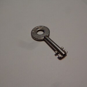 May include: A silver key with a round head and a single row of teeth. The key has the word "DEFEX" engraved on the head.
