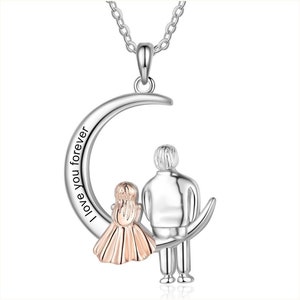 Peut inclure: Un collier pendentif argenté représentant un croissant de lune avec deux personnages. Les mots "I love you forever" sont inscrits sur la lune. Une femme en robe et un homme sont représentés.