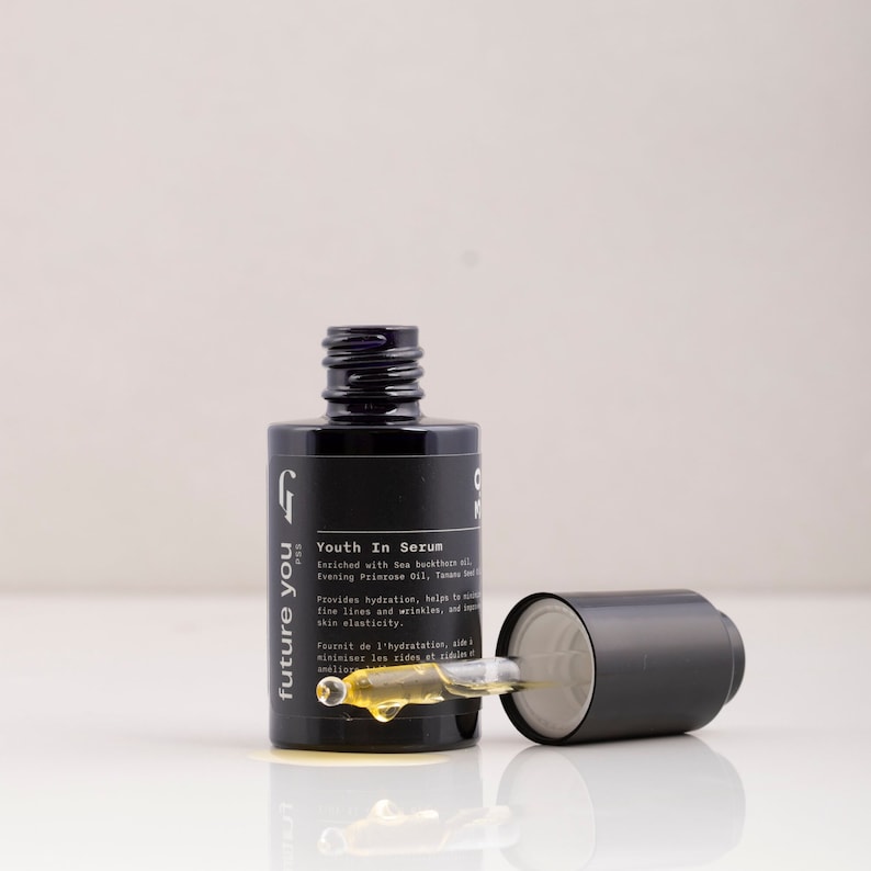 May include: A black glass bottle with a dropper, labeled "future you" and "Youth In Serum". The bottle contains a yellow liquid and is sitting on a white surface.