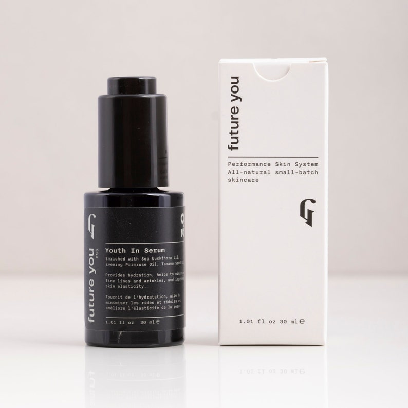 May include: A black glass bottle with a dropper top containing a serum called "Youth In Serum" by the brand "future you". The bottle is labeled with the text "Enriched with Sea buckthorn oil, Evening Primrose Oil, Tamanu Seed Oil, Rose Oil" and "Provides hydration, helps to minimize fine lines and wrinkles, and improve skin elasticity". The bottle is sitting on a white surface next to a white box with the same branding and text. The box is labeled with the text "Performance Skin System, All-natural small-batch skincare".