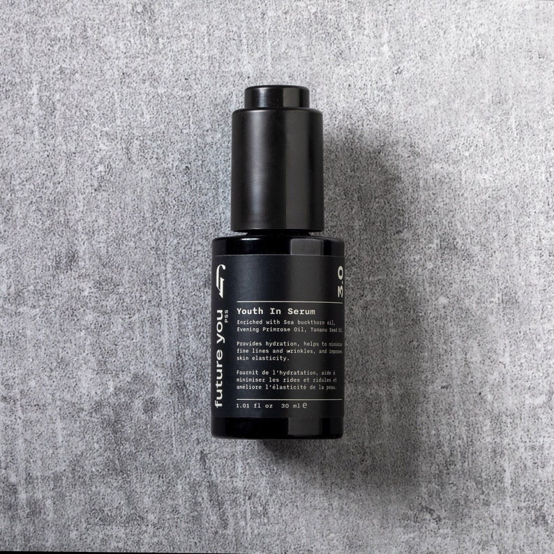 May include: A black glass bottle of serum labeled "future you PSS Youth In Serum" with a dropper top. The bottle is on a gray textured background. The serum is enriched with Sea Buckthorn oil, Evening Primrose Oil, and Tamanu Seed Oil. It provides hydration, helps to reduce fine lines and wrinkles, and improves skin elasticity. The bottle contains 1.01 fl oz or 30 ml of serum.