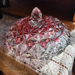 May include: A clear glass candy dish with a red, diamond-shaped pattern and a crystal knob on the lid.