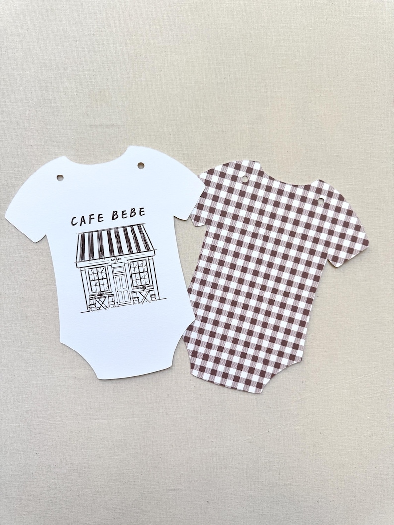 May include: Two baby bodysuit-shaped paper cutouts. One is white with a black and white cafe illustration and the text "CAFE BEBE". The other is brown and white gingham.