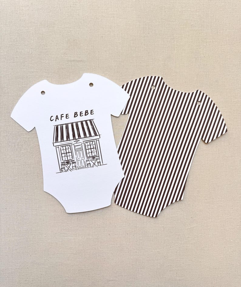 May include: Two baby bodysuit-shaped paper cutouts. One is white with a black and white cafe illustration and the text "CAFE BEBE". The other is a black and white striped pattern.