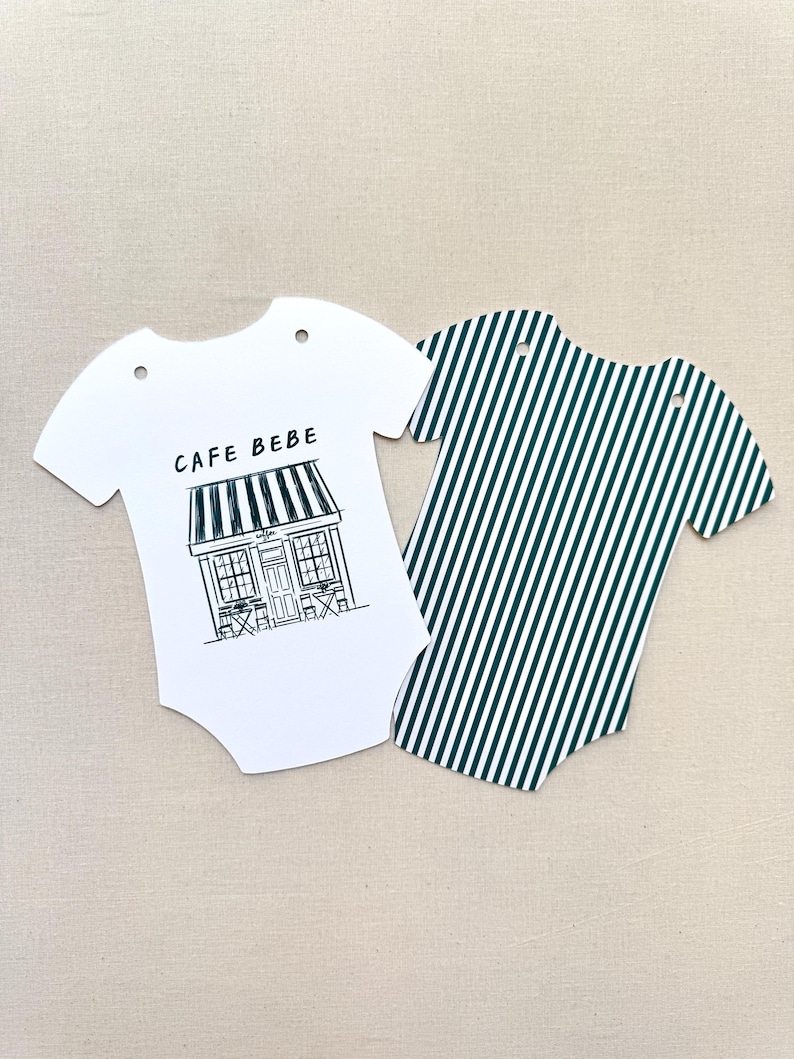 May include: Two baby bodysuit-shaped paper cutouts. One is white with a black and white cafe illustration and the text "CAFE BEBE". The other is green and white striped.