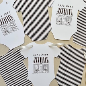 May include: White baby bodysuit-shaped tags with black and white striped patterns and the text "CAFE BEBE". Some tags feature a cafe illustration. Each tag has a hole for ribbon.