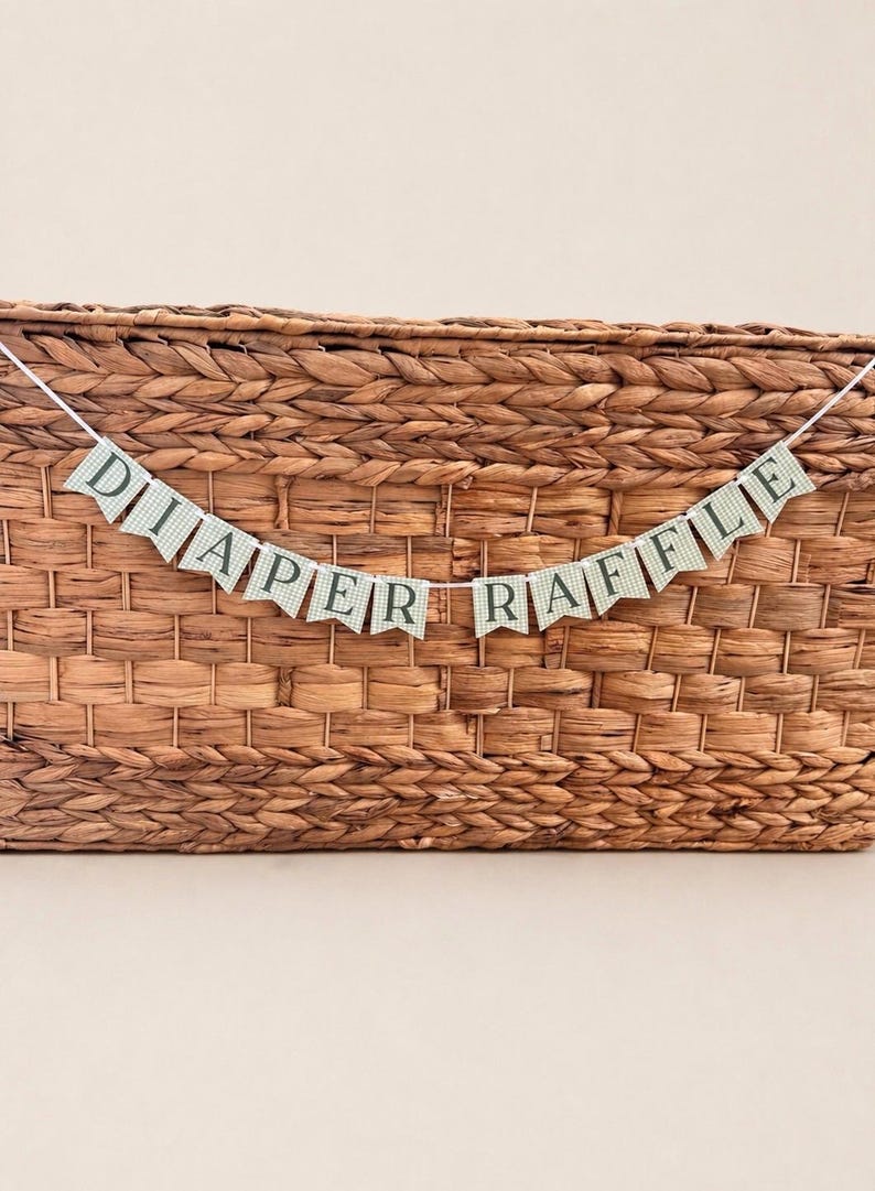 K&ouml;nnte beinhalten: Ein Banner mit der Aufschrift "DIAPER RAFFLE" auf kleinen, gr&uuml;n-wei&szlig; karierten F&auml;hnchen. Es ist &uuml;ber einem geflochtenen Korb gespannt und eignet sich als festliche Dekoration f&uuml;r eine Babyparty oder &auml;hnliche Veranstaltung.