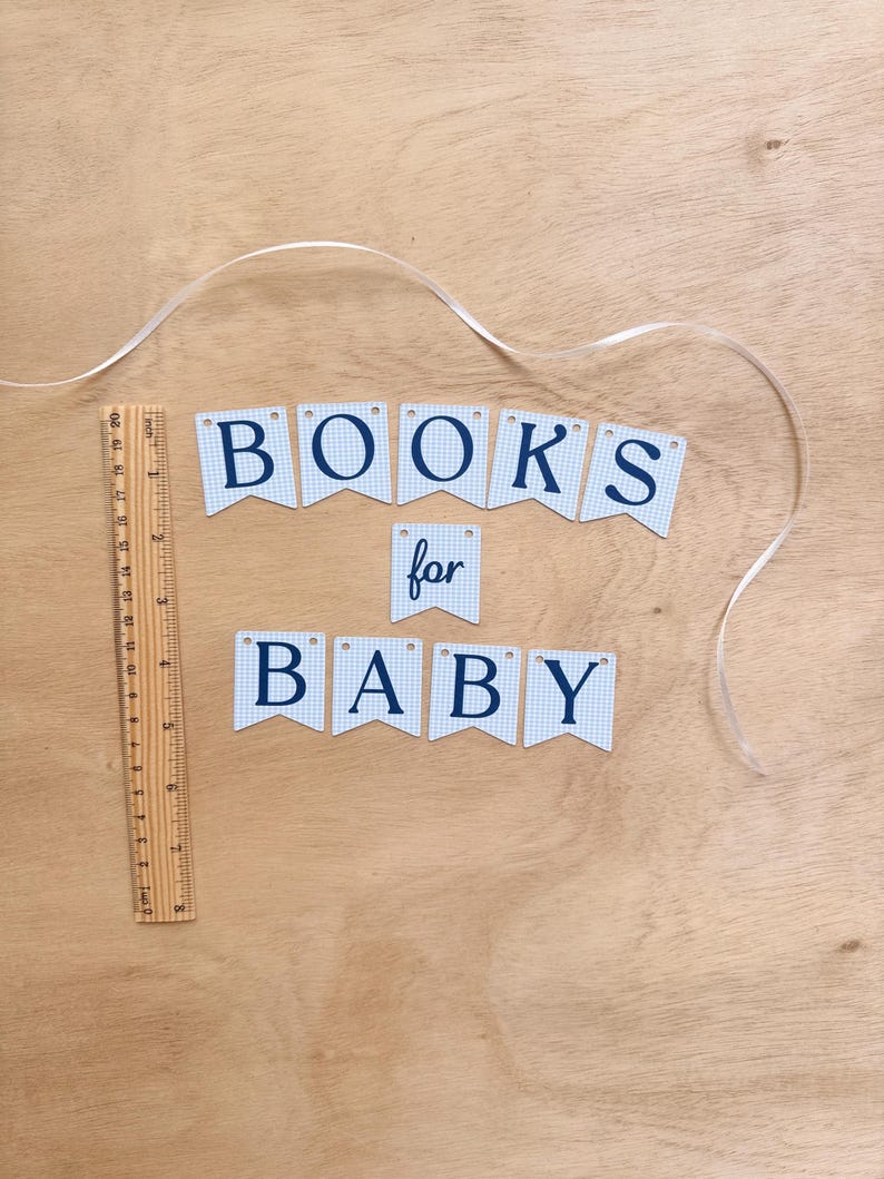 K&ouml;nnte beinhalten: Ein Banner mit der Aufschrift "BOOKS for BABY" in dunkelblauen Buchstaben auf hellblau-wei&szlig; kariertem Hintergrund. Ein Holzlineal liegt neben dem Banner, und ein wei&szlig;es Band ist &uuml;ber die Holzoberfl&auml;che drapiert.