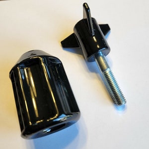 May include: Two black plastic knobs with a threaded metal shaft. One knob has a star-shaped design and the other has a cylindrical shape.