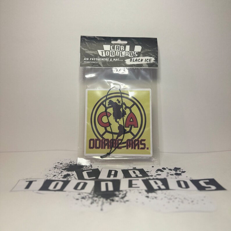 May include: A square car air freshener with a yellow background and a black and white logo. The logo is a circle with a black outline and a white letter "C" and "A" inside. The text "ODIARE MAS." is written in red below the logo.