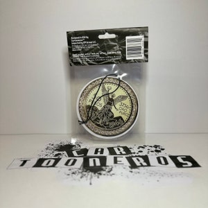 Pu&ograve; includere: Un profumatore per auto dorato a forma di moneta messicana da 50 pesos con la scritta "37.5G ORO PURO 1946" e la raffigurazione di un angelo. Il profumatore &egrave; circondato da un anello di strass.