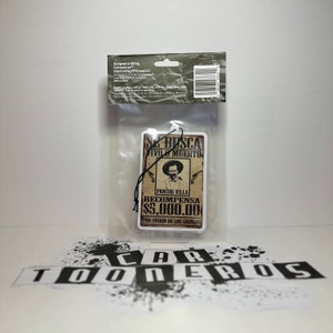 May include: A brown and white car air freshener with a vintage wanted poster design. The poster features a drawing of a man with a mustache and a hat, and the text "Se Busca Vivo o Muerto Pancho Villa Recompensa $5,000.00 Por Orden de los Gringos".