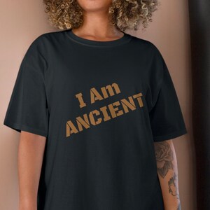 May include: A black t-shirt with the text "I AM ANCIENT" printed in brown on the front.