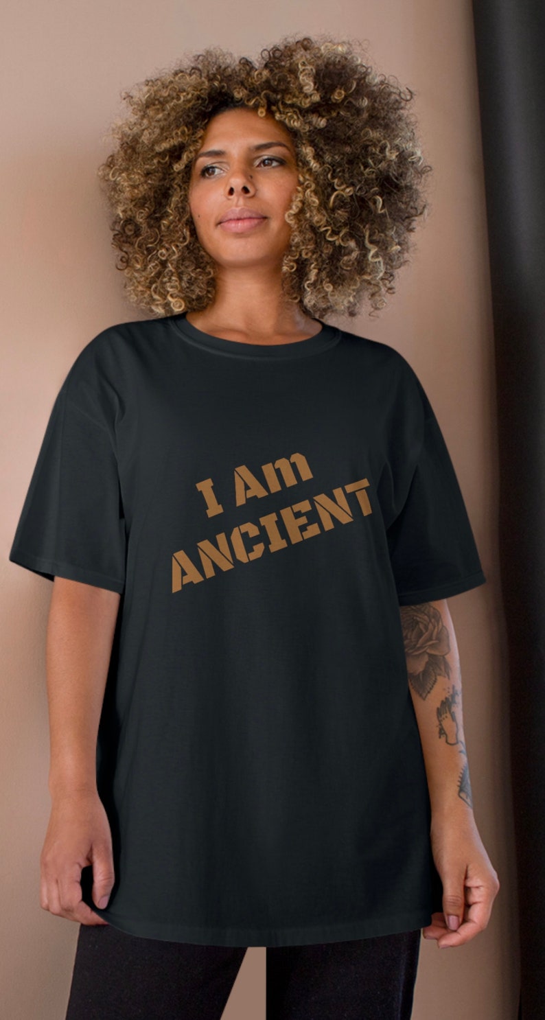 May include: A black t-shirt with the text "I AM ANCIENT" printed in brown on the front.