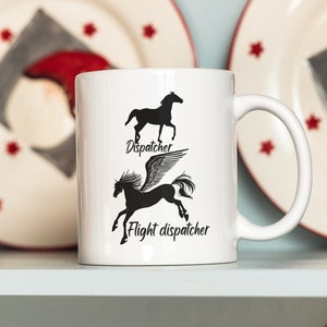 May include: White ceramic mug with a black silhouette of a horse and a winged horse with the text "Dispatcher" and "Flight dispatcher". The mug is on a shelf with other mugs and plates with a Christmas theme.