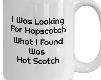 May include: White ceramic coffee mug with black text that reads "I was looking for hopscotch what I found was hot scotch".