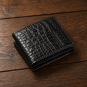May include: A black bifold wallet featuring a textured crocodile skin pattern. The wallet has a glossy finish and a rectangular shape with rounded corners, showing a folded design with visible layered edges along the side of the accessory.