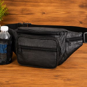 May include: A black leather fanny pack featuring multiple zippered compartments, an adjustable black nylon strap with a plastic buckle, and an attached black mesh water bottle holder containing a clear plastic water bottle with a white cap.