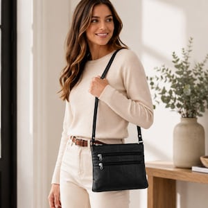 May include: A black rectangular crossbody bag featuring three horizontal zippered pockets on the front, a thin adjustable shoulder strap, and silver-toned metal zipper pulls. The bag is constructed with a smooth, matte finish material.