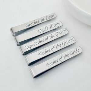 May include: Five silver tie clips with different engraved text: "Brother-in-Law", "Uncle Harry", "Step-Father of the Groom", "Father of the Groom", and "Father of the Bride".