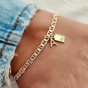 May include: Gold ankle bracelet with a charm featuring the letter 'A' and a heart.