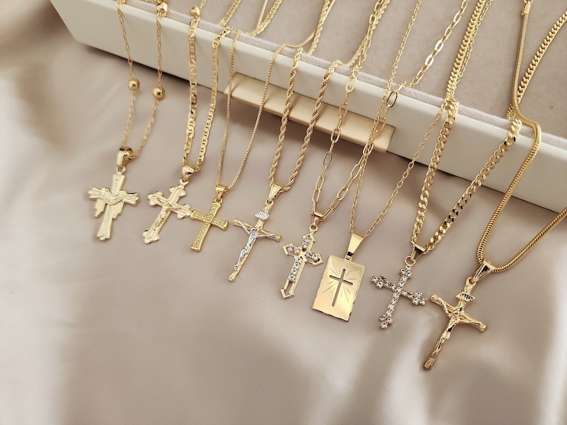May include: A set of nine gold chain necklaces with different cross pendants. The crosses are all gold and have various designs, including a simple cross, a cross with a crown, and a cross with a heart.