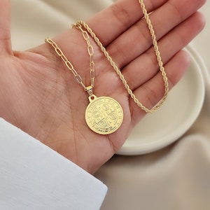 May include: A gold chain necklace with a large, round, gold pendant featuring a detailed design. The pendant is a Saint Christopher medal.
