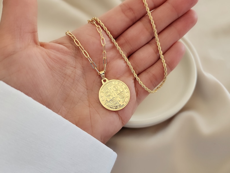 May include: A gold chain necklace with a large, round, gold pendant featuring a detailed design. The pendant is a Saint Christopher medal.