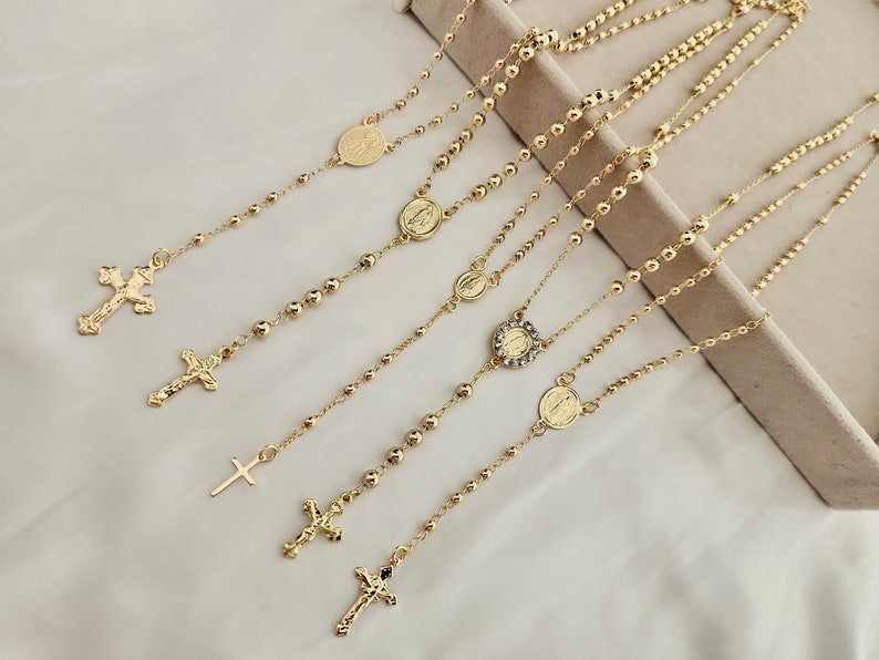 May include: Five gold-tone necklaces with cross and religious medal pendants. Each necklace features a beaded chain with a different pendant.