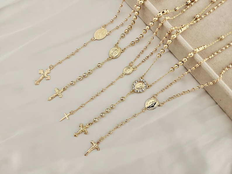 May include: Five gold chain necklaces with religious pendants, including crosses and medallions. The chains are layered and feature small beads.