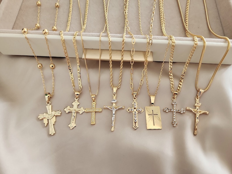 May include: Nine gold chain necklaces with different cross pendants. Some of the crosses are plain, while others have small stones or engravings. The chains are all different styles, including rope, curb, and box chains.
