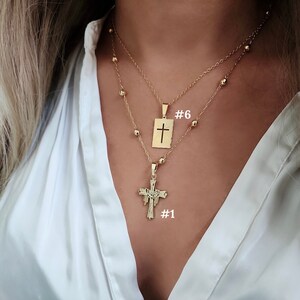 May include: Two gold necklaces with cross pendants. The top necklace has a simple cross pendant with the number "#6" written next to it. The bottom necklace has a more ornate cross pendant with the number "#1" written next to it.