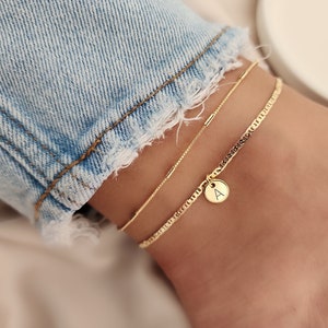 Op de afbeelding: Gouden enkelbandje met een delicate ketting en een bedel met de letter 'A'.