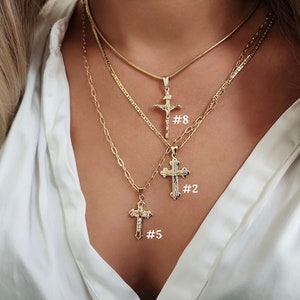 May include: Three gold chain necklaces with different cross pendants. The top necklace has a simple cross pendant, the middle necklace has a more ornate cross pendant, and the bottom necklace has a cross pendant with small clear stones. The necklaces are labelled with numbers 8, 2, and 5.