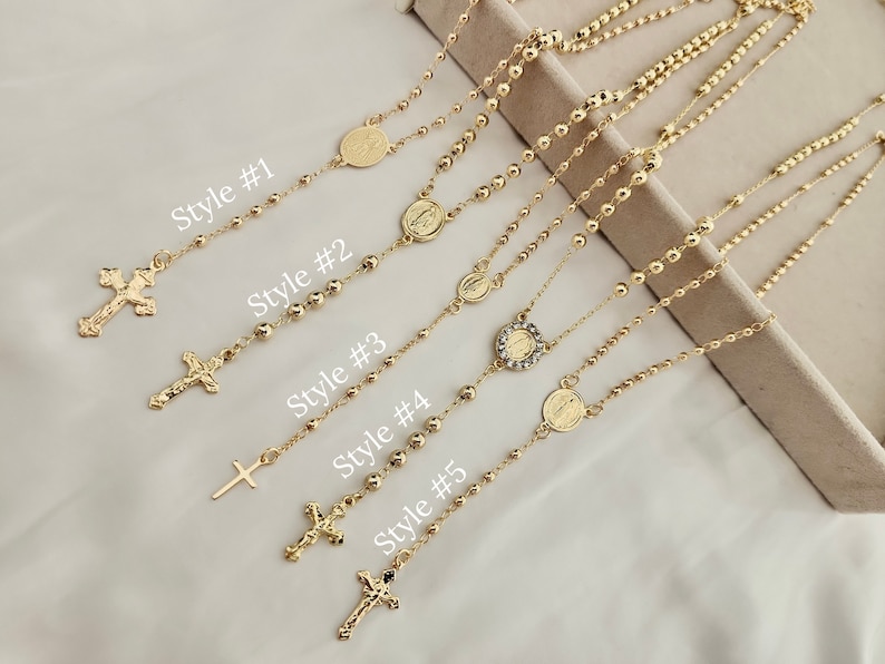May include: Five gold-toned necklaces with different religious pendants. The pendants include a cross, a heart with a rhinestone, and a Virgin Mary. The necklaces are labelled with the text "Style #1", "Style #2", "Style #3", "Style #4", and "Style #5".