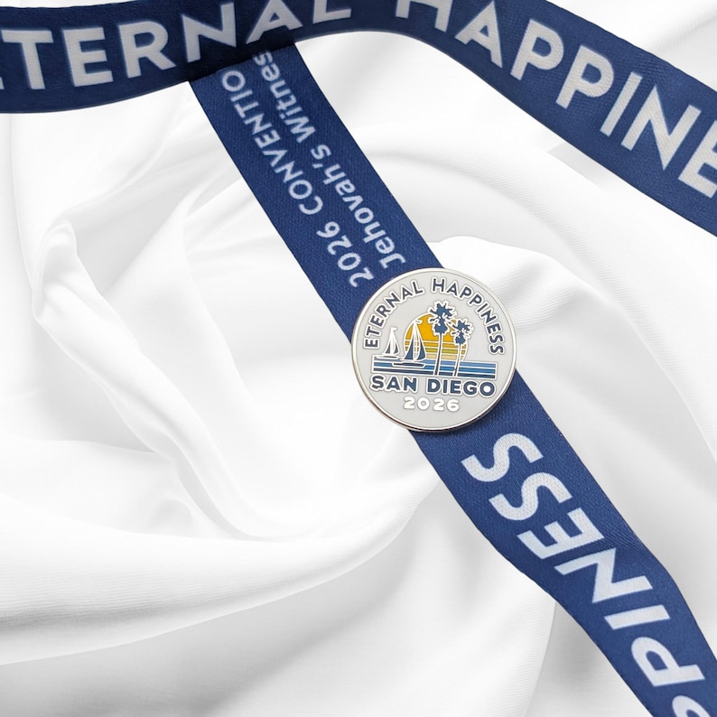 May include: A silver commemorative coin with the text "Eternal Happiness" and "San Diego 2026" is displayed on a blue ribbon. The ribbon also features the text "2026 Convention Jehovah's Witnesses". The background is white fabric.