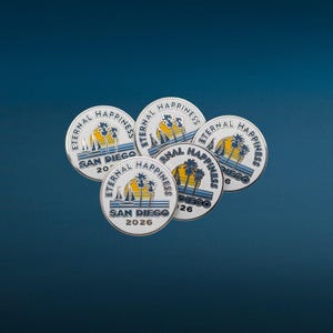 May include: Five round metal pins with a white background and a blue border. Each pin features a sailboat, palm trees, and the words "Eternal Happiness" and "San Diego" with a year. The pins are arranged on a dark blue surface.