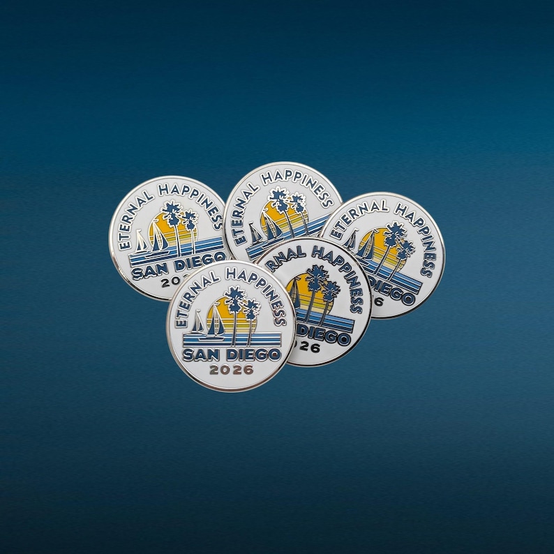 May include: Five round metal pins with a white background and a blue border. Each pin features a sailboat, palm trees, and the words "Eternal Happiness" and "San Diego" with a year. The pins are arranged on a dark blue surface.