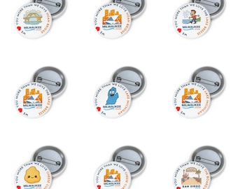 May include: A collection of nine white pin-back buttons with various designs and the text "You More Than We Love Milwaukee". Each button features a different graphic, including a bridge, cityscape, and cheese curds. The buttons are round and have a metal backing.