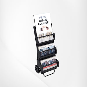 May include: A black portable literature display stand with three tiered shelves, featuring wheels and a handle at the base. The stand holds various brochures and booklets, including a prominent sign at the top that reads FREE BIBLE COURSE.