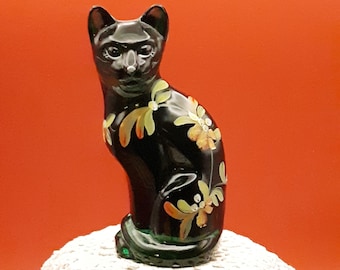 Peut inclure: Une figurine de chat en verre noir avec des fleurs peintes en vert et or. Le chat est assis, la queue enroulée autour de ses pattes.