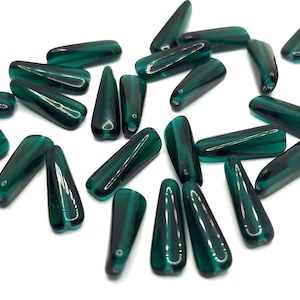 May include: A selection of dark green, teardrop-shaped beads with a glossy finish. The beads are scattered on a white surface, highlighting their elongated form and translucent quality. These beads are suitable for jewellery making.