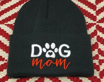 May include: Gray knit beanie with white embroidered text "DOG" with a white paw print and a red heart in the center of the paw print. The text "mom" is embroidered in orange below the paw print.
